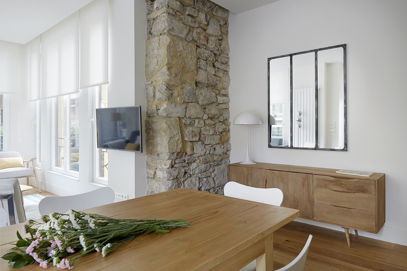 Detalle del salón con pared de piedra, espejo industrial y mueble de madera