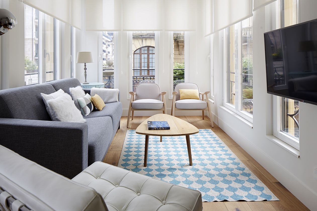 Salón con sofá gris, butacas de madera y alfombra geométrica azul