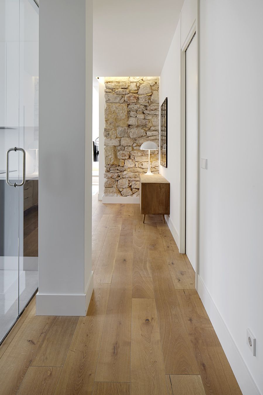 Pasillo con suelo de madera noble y pared de piedra iluminada al fondo